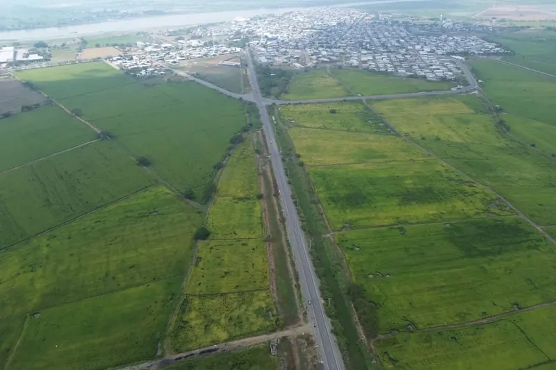 Vista aérea de un predio agrícola dividido en lotes junto a una carretera, con un poblado y un río al fondo